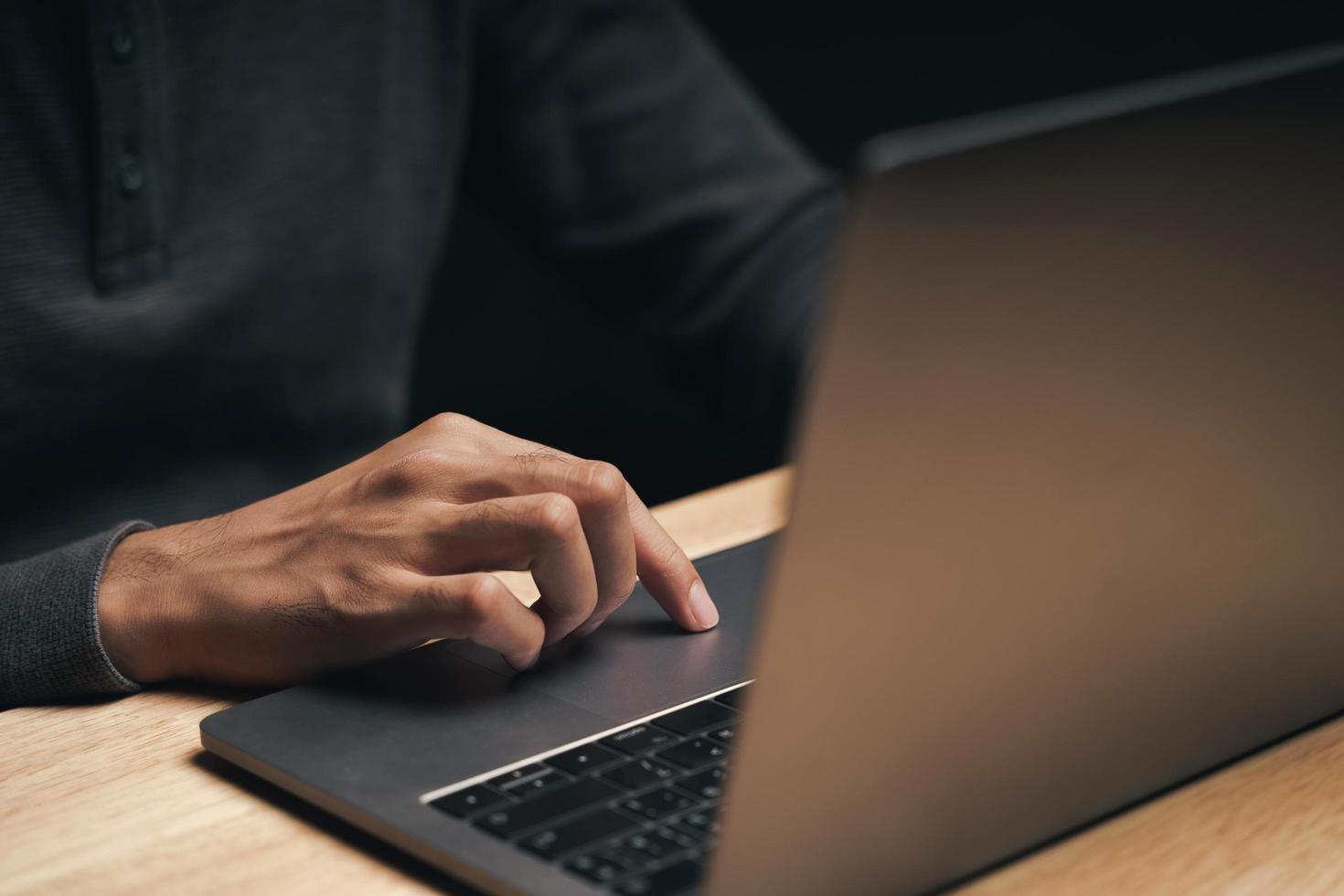 Hombre usando una computadora portátil en la mesa de madera, buscando, navegando foto