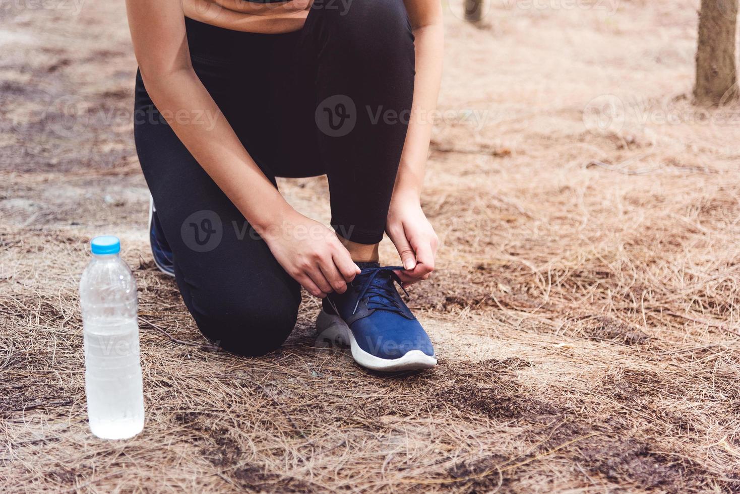 Mujer atar los cordones de los zapatos para correr en el bosque con una botella de agua potable foto