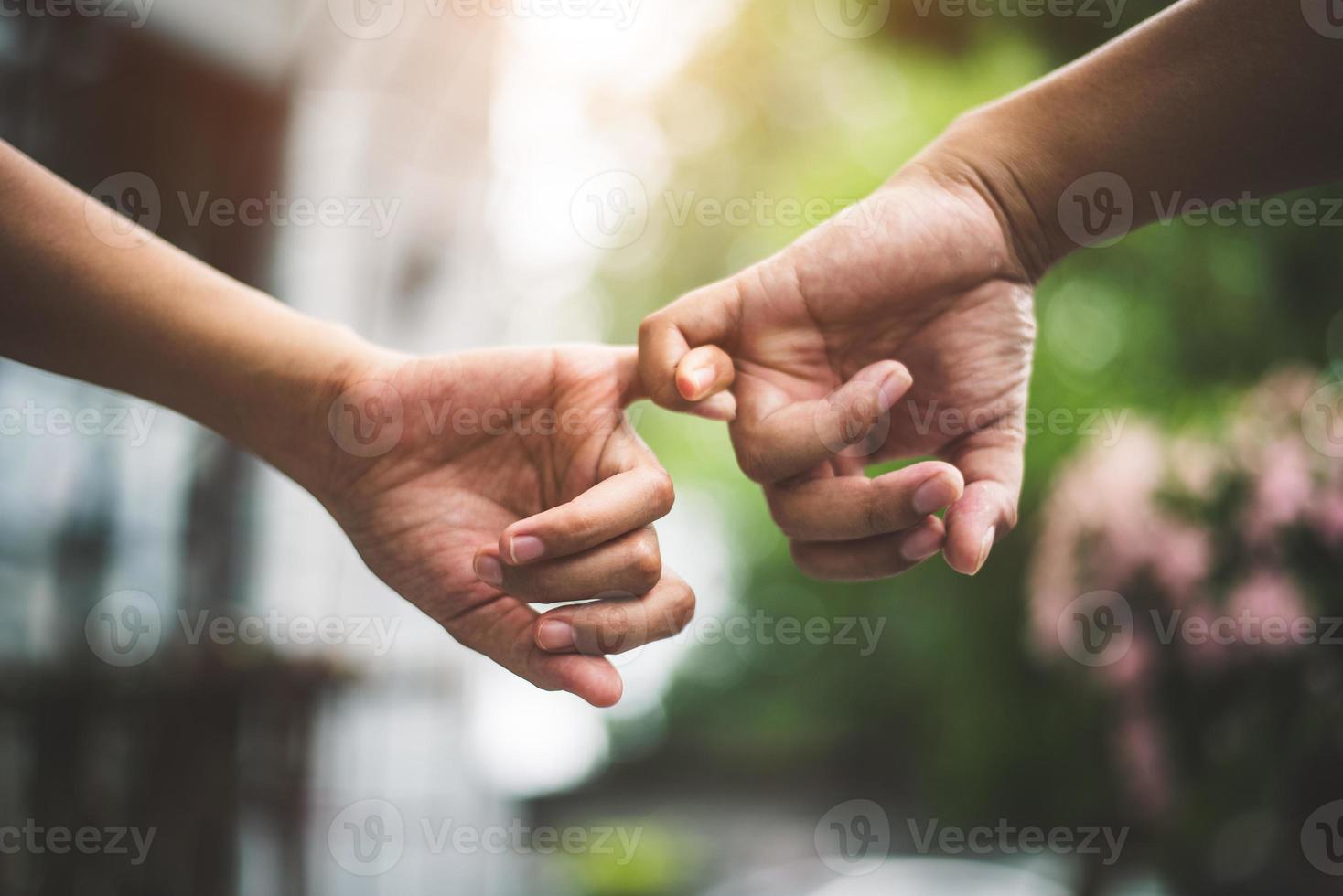 Close up couple holding pinkies fingers  in park as swear and promise photo