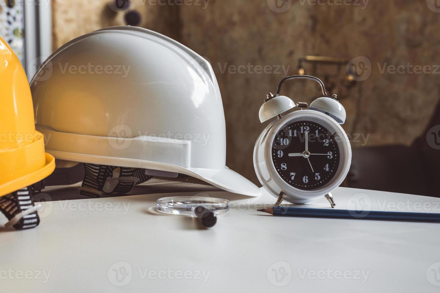 Cerca del reloj y el casco de seguridad de ingeniería en la tabla de planos foto