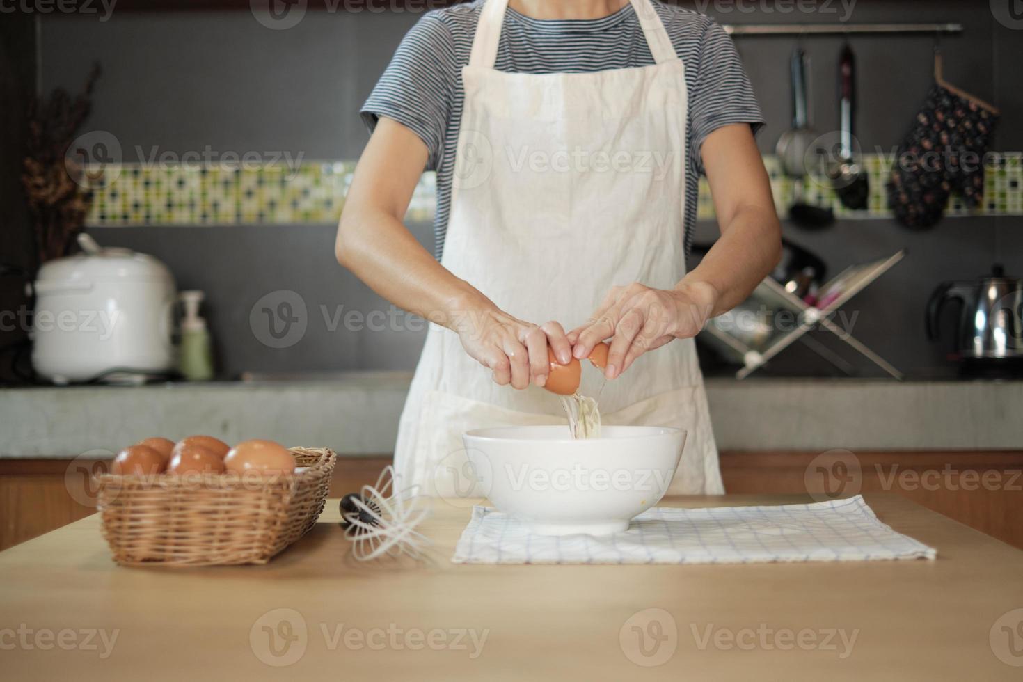 cocinera con un delantal blanco está rompiendo un huevo en la cocina de casa. foto