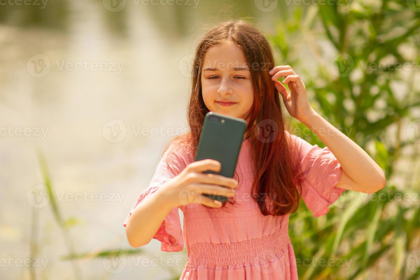 Portrait of a young girl making selfie photo near the river in summer.