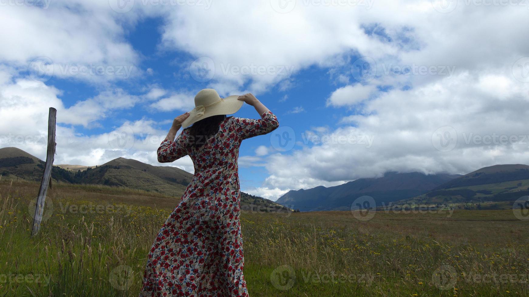 Woman in floral dress holding her long hat with her hands walking photo