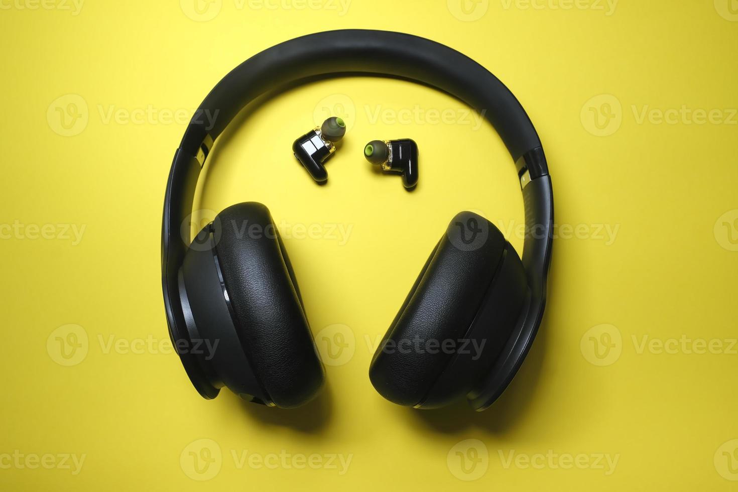 Black headphone and tiny earbuds on yellow background photo