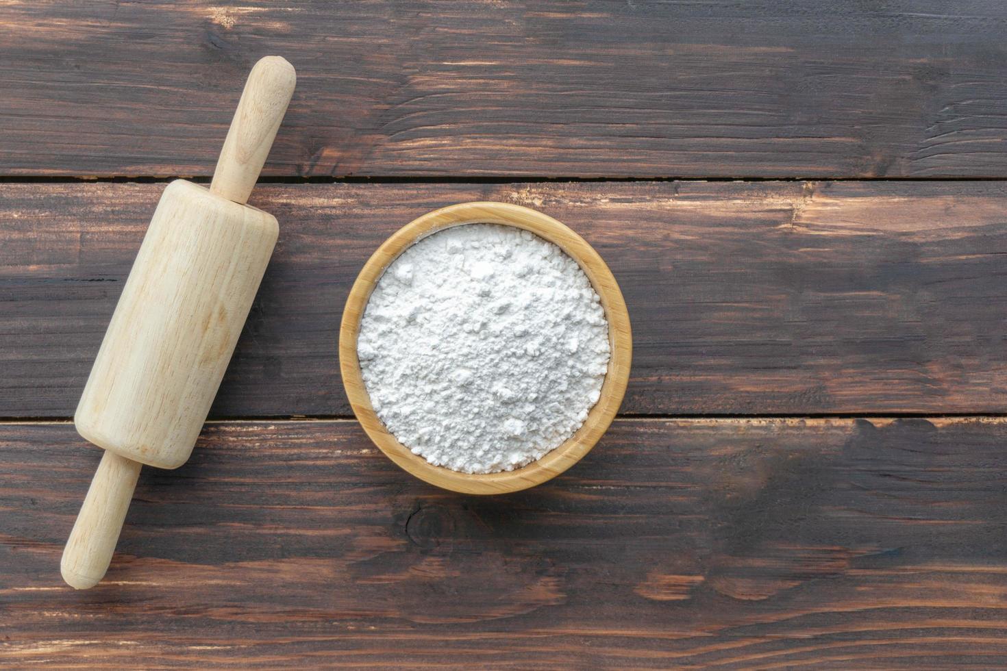 Rolling pin and flour in bowl on wooden table photo
