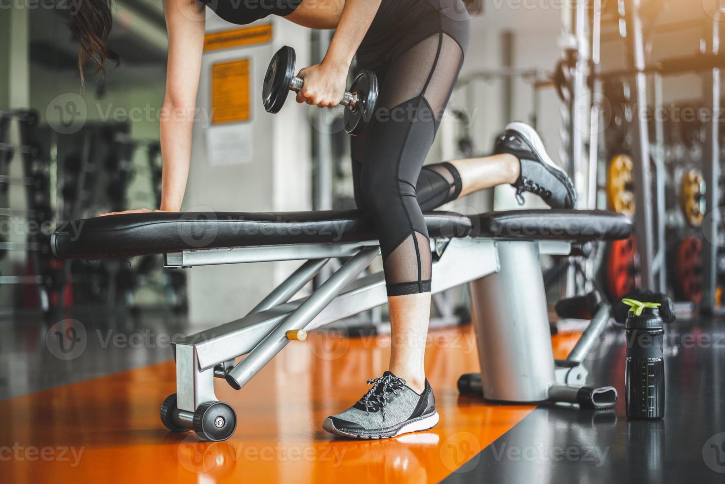 Young woman bench pressing with dumbbells in fitness gym photo