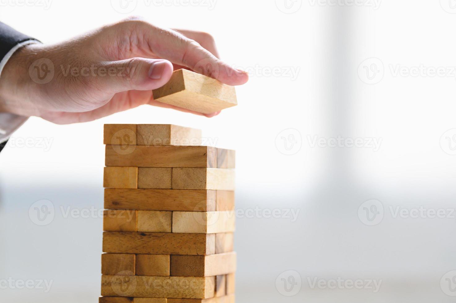 Businessman arranging wood block and stacking as tower by hand photo