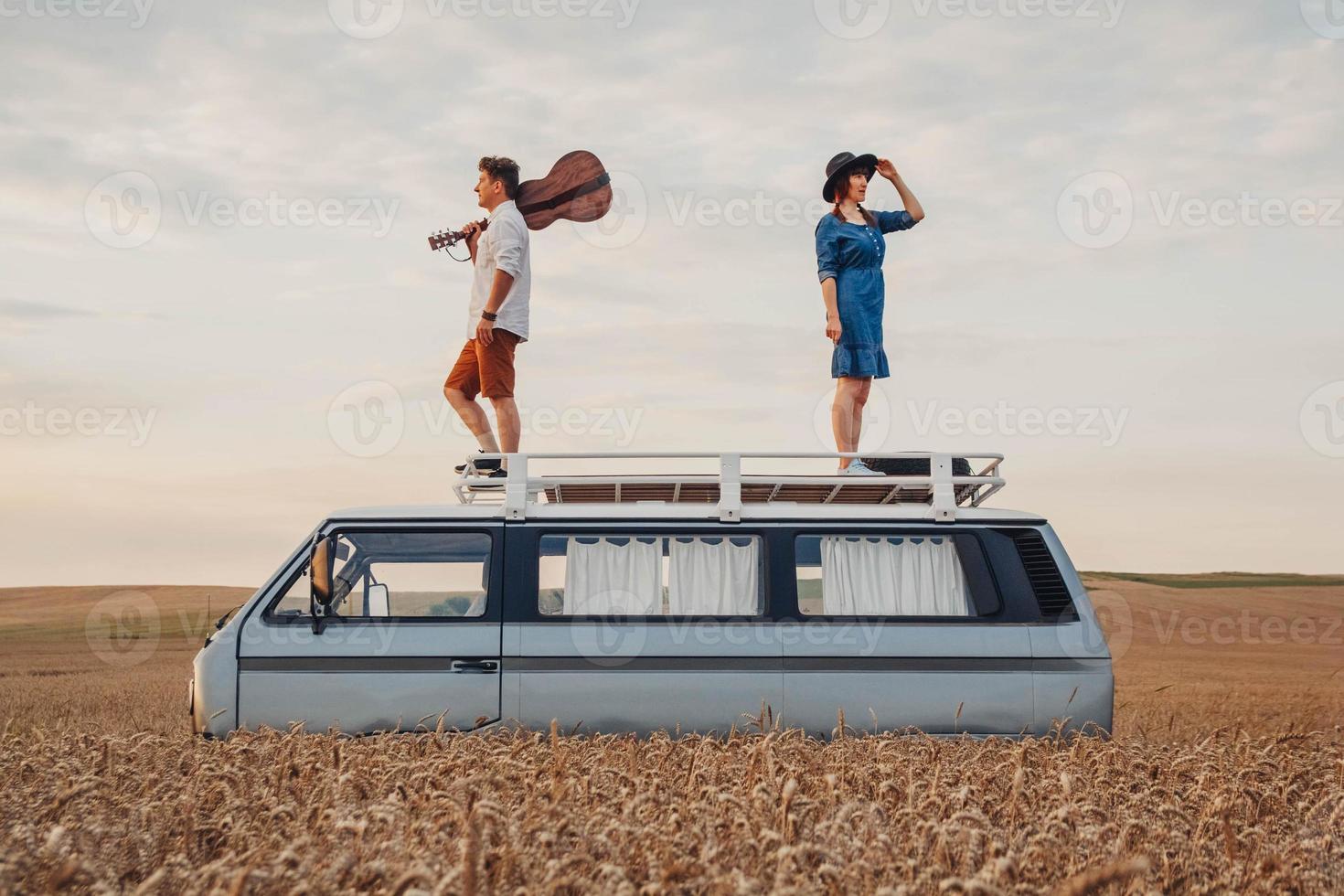 man with a guitar and woman are standing on roof of a car in a wheat photo