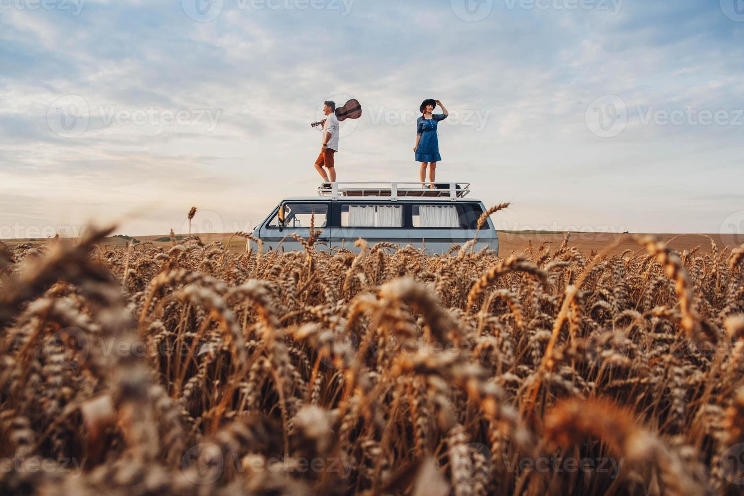 Hombre con una guitarra y una mujer de pie en el techo de un coche en un campo de trigo foto