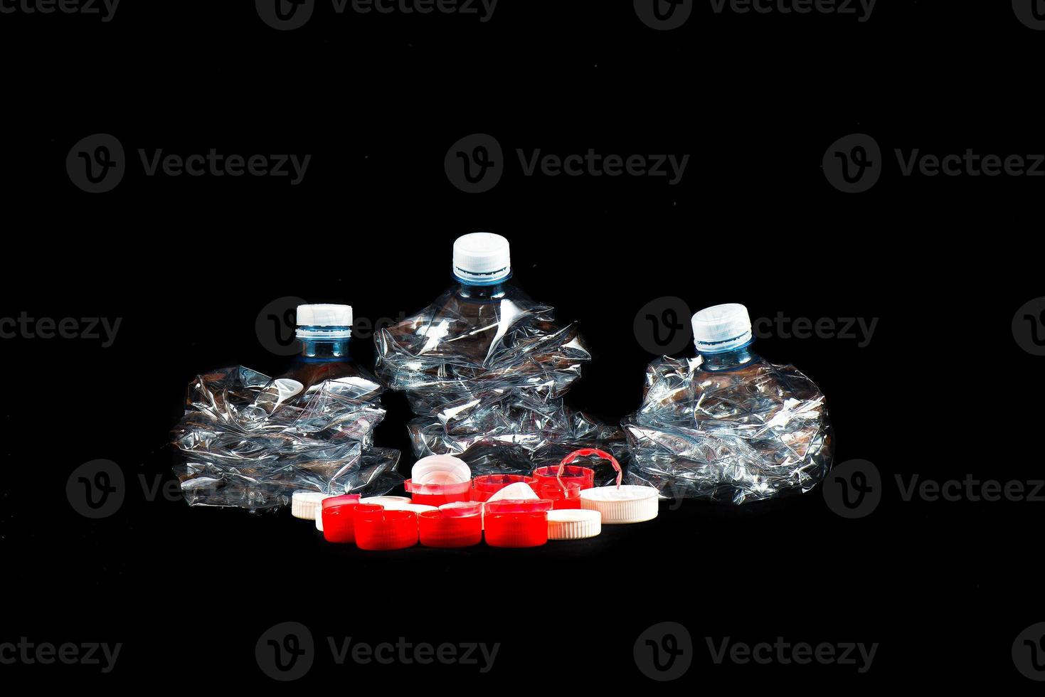 Botellas de plástico transparente trituradas y tapones sobre un fondo negro. foto