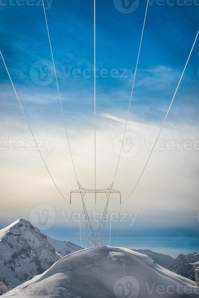 Pylons covered with snow in the high mountains carry energy downstream photo