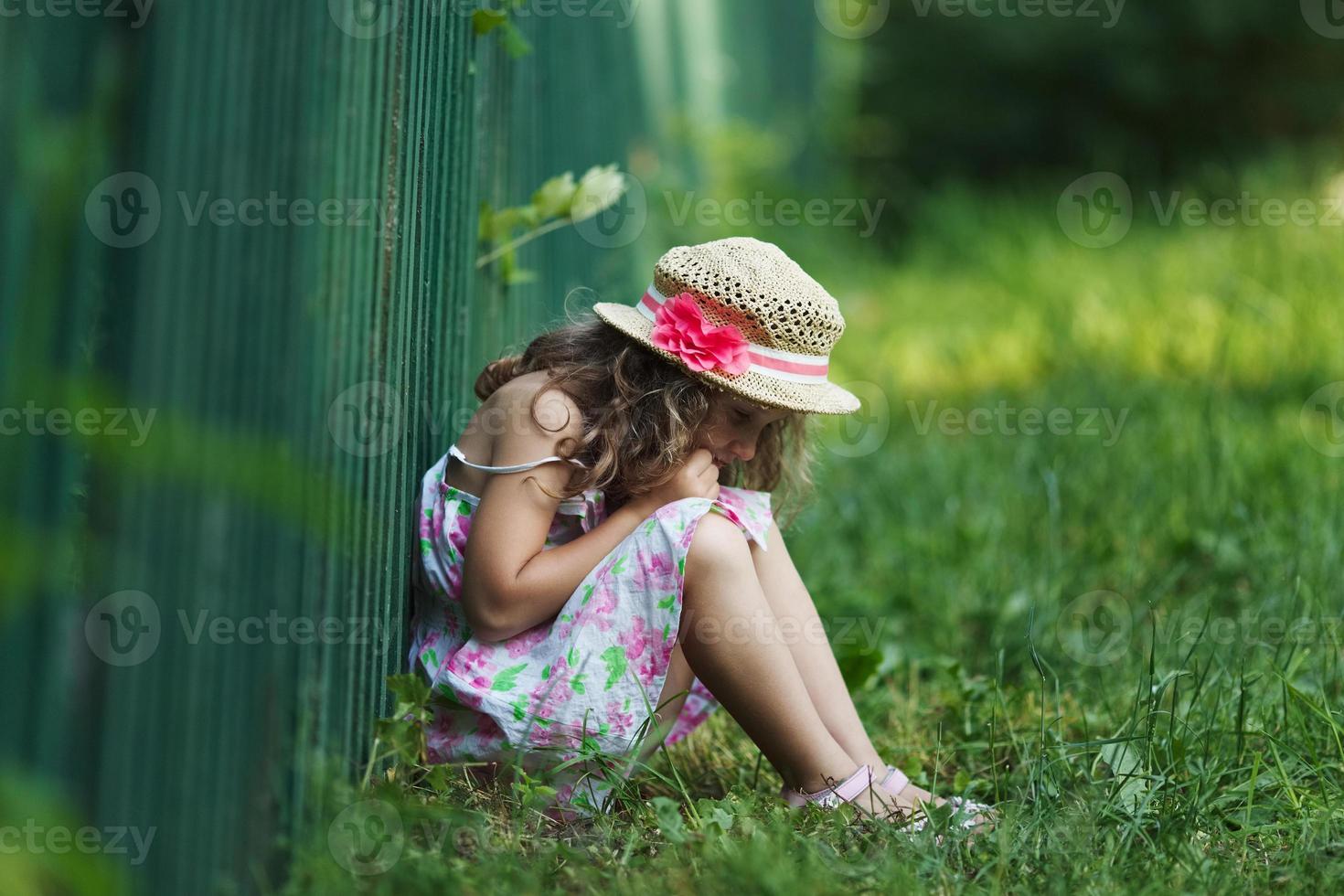 Sad little girl sitting on grass photo