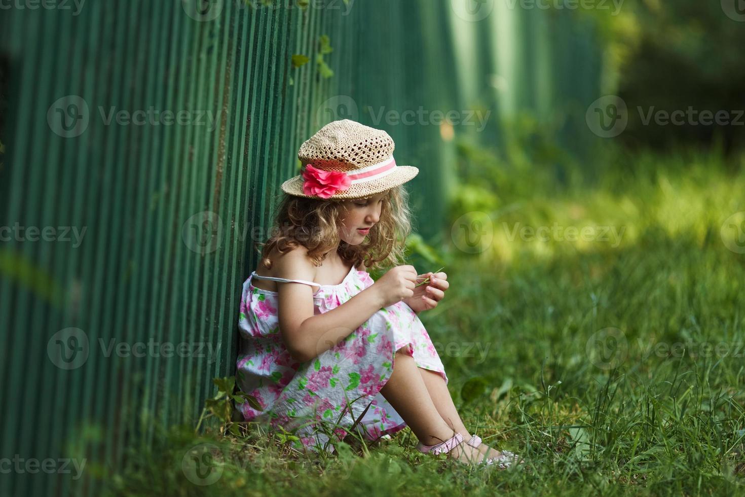 niña sentada apoyada contra una valla foto