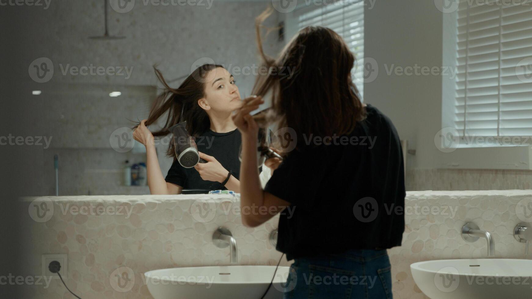 Woman using hairdryer in bathroom looking in mirror photo