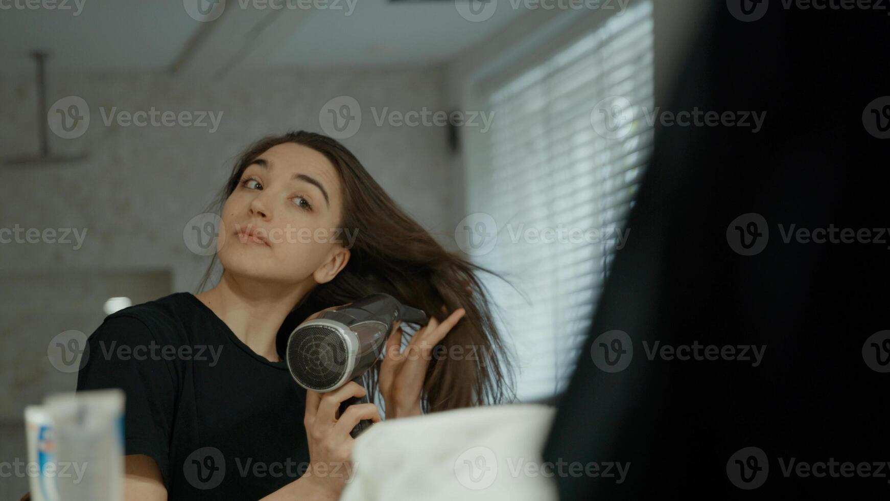 Woman using hairdryer in bathroom looking in mirror photo