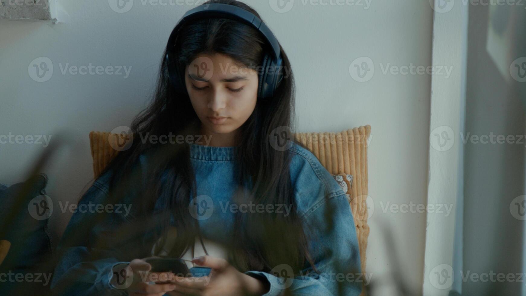 Girl with headphone sitting in corner whilst typing on smartphone photo