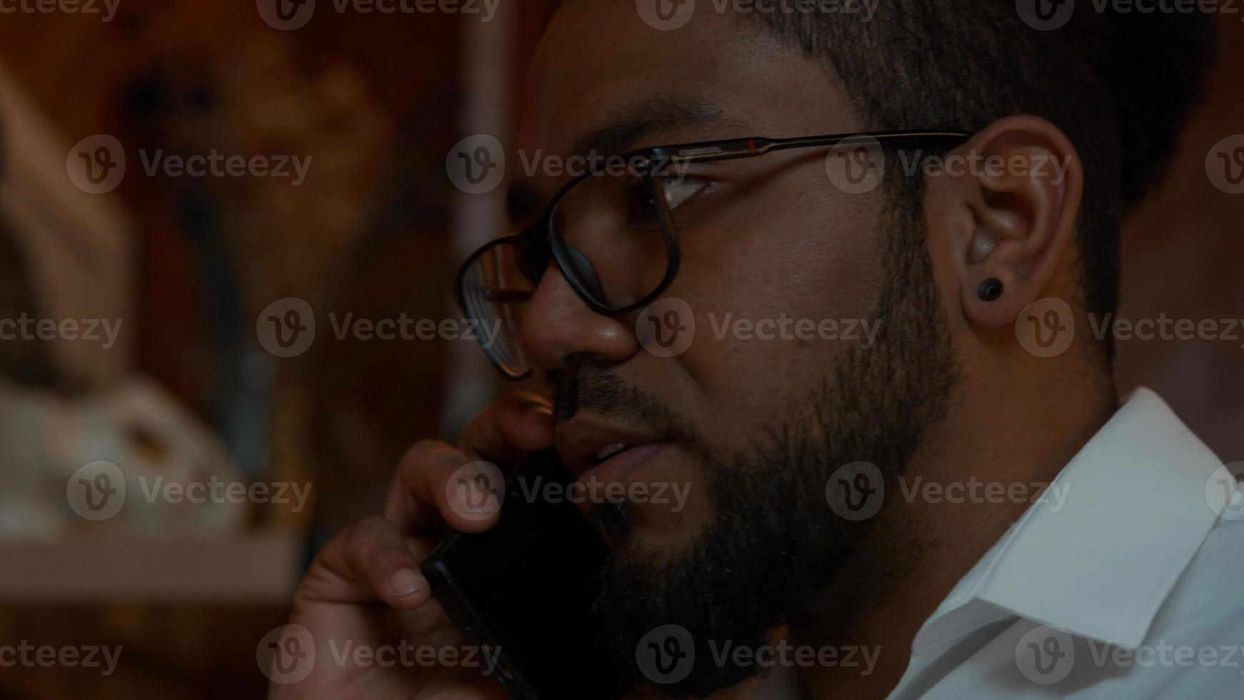 Close up of black man wearing glasses, mobile phone on ear, talking photo