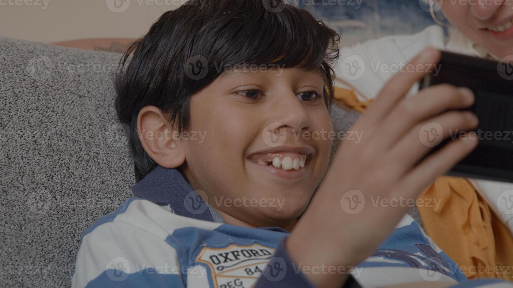 Boy playing with game console and woman watching on couch photo