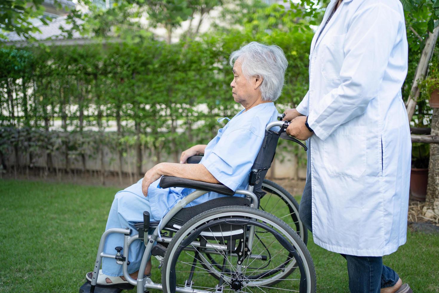 Médico ayuda a paciente anciana asiática sentada en silla de ruedas en el parque foto
