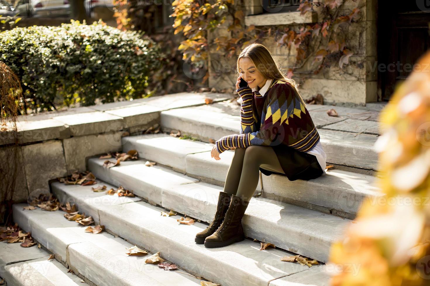 Young woman sitting on a stairs with mobile phone in autumn park photo