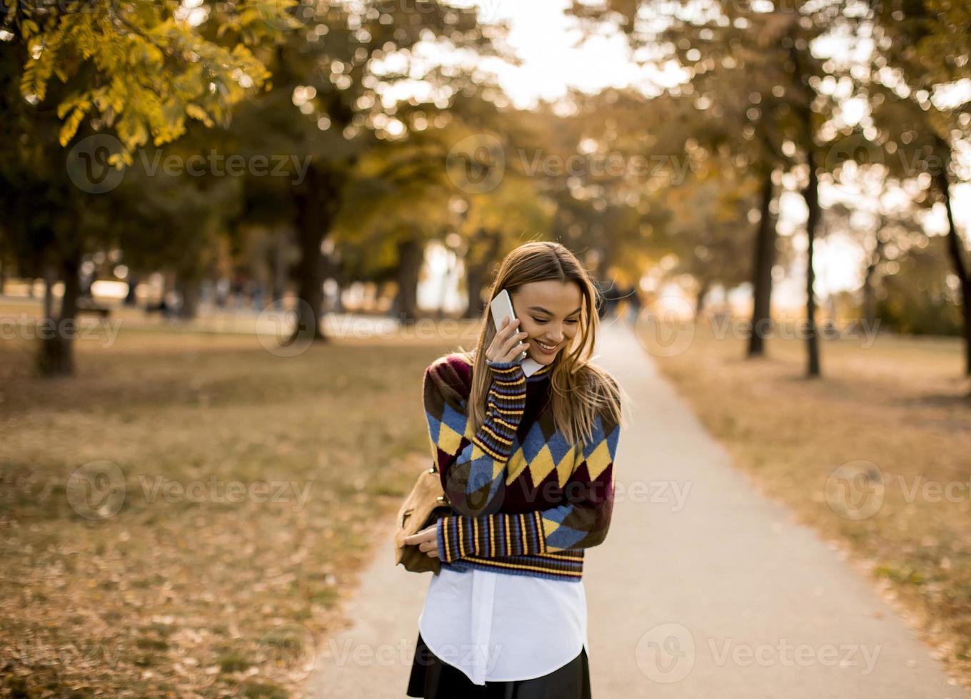 Pretty young woman walking in autumn park and using a mobile phone photo