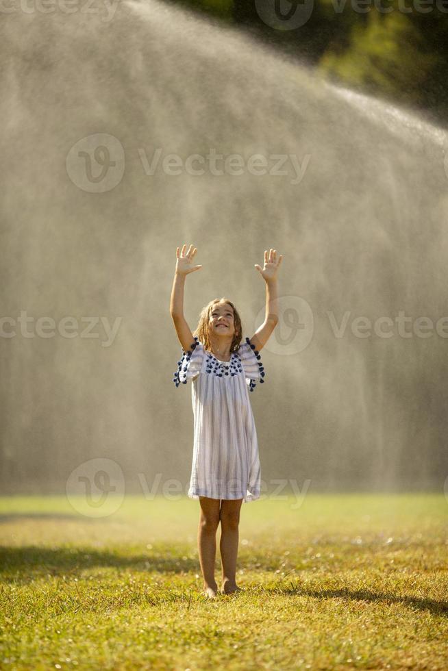 Cute little girl having fun under irrigation sprinkler photo