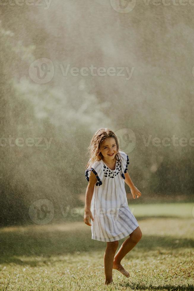 Cute little girl having fun under irrigation sprinkler photo