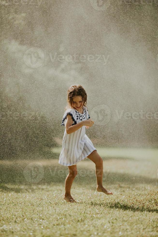 Cute little girl having fun under irrigation sprinkler photo