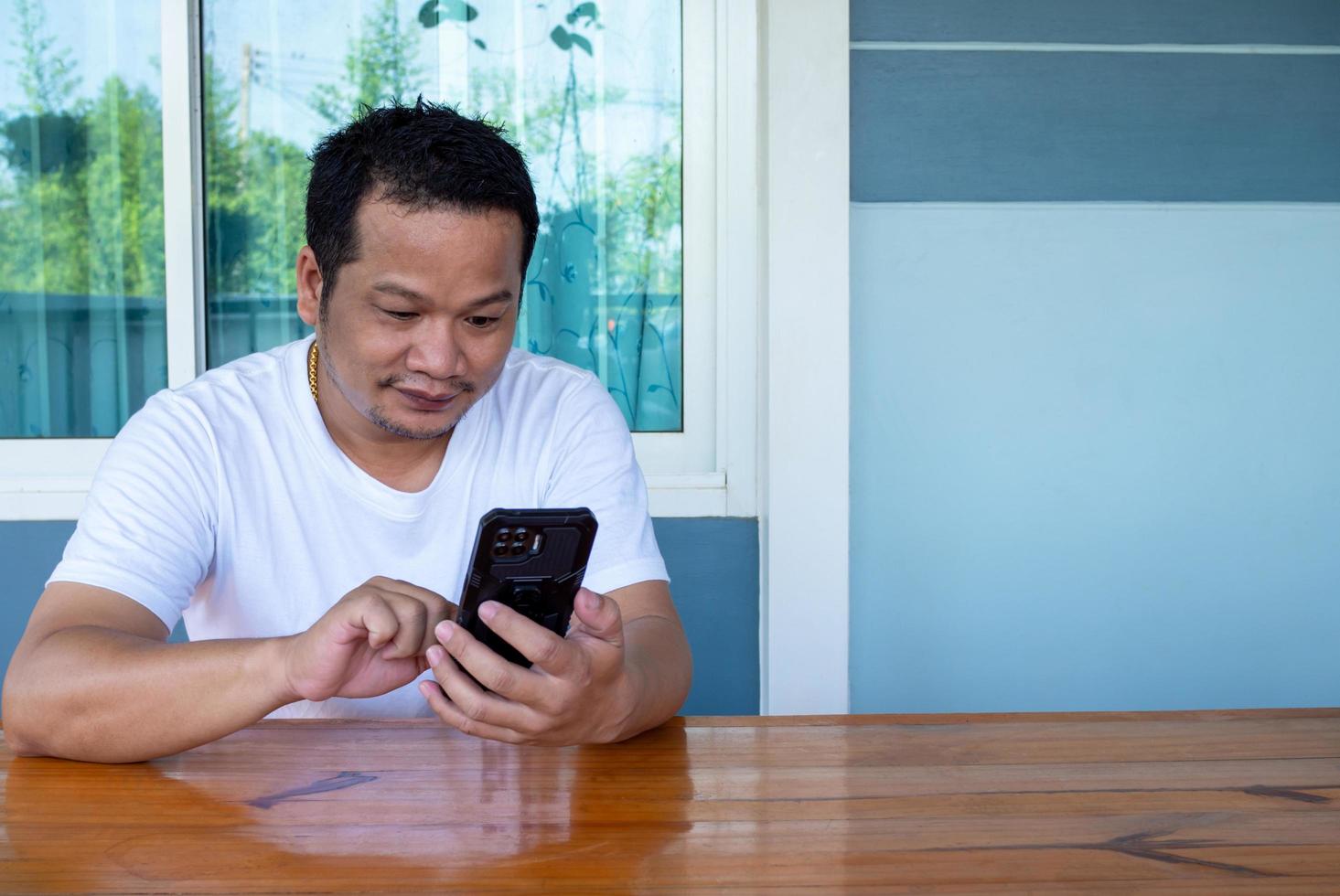 Hombre asiático vestido con camisa blanca usando el teléfono en una mesa de madera foto