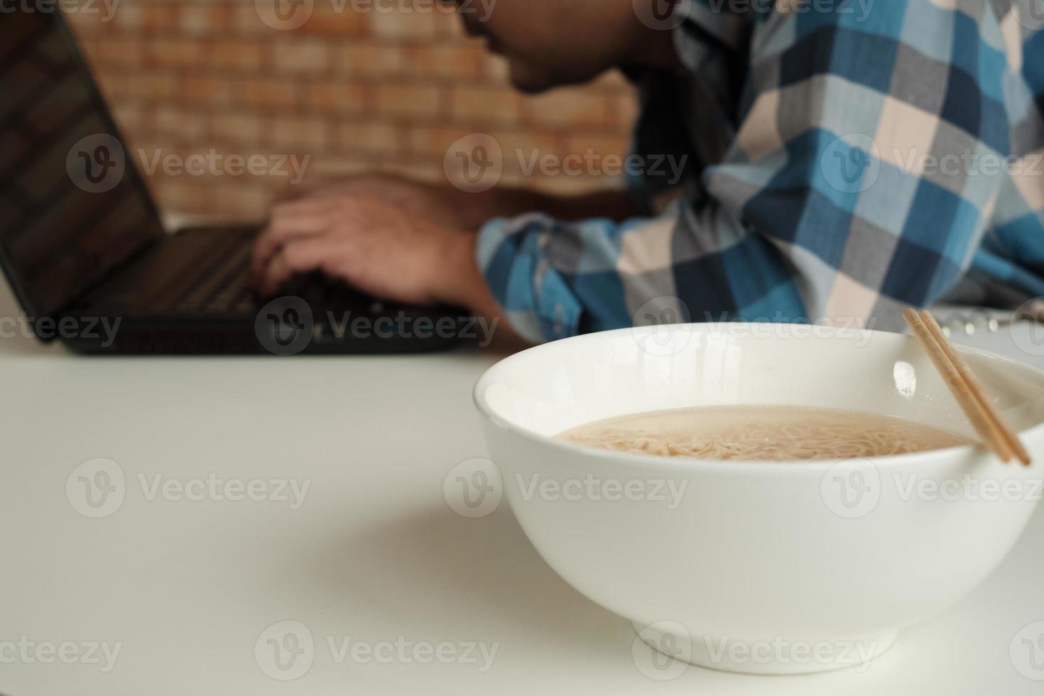 El trabajador asiático come apresuradamente fideos instantáneos en el ajetreado trabajo de horas extra. foto