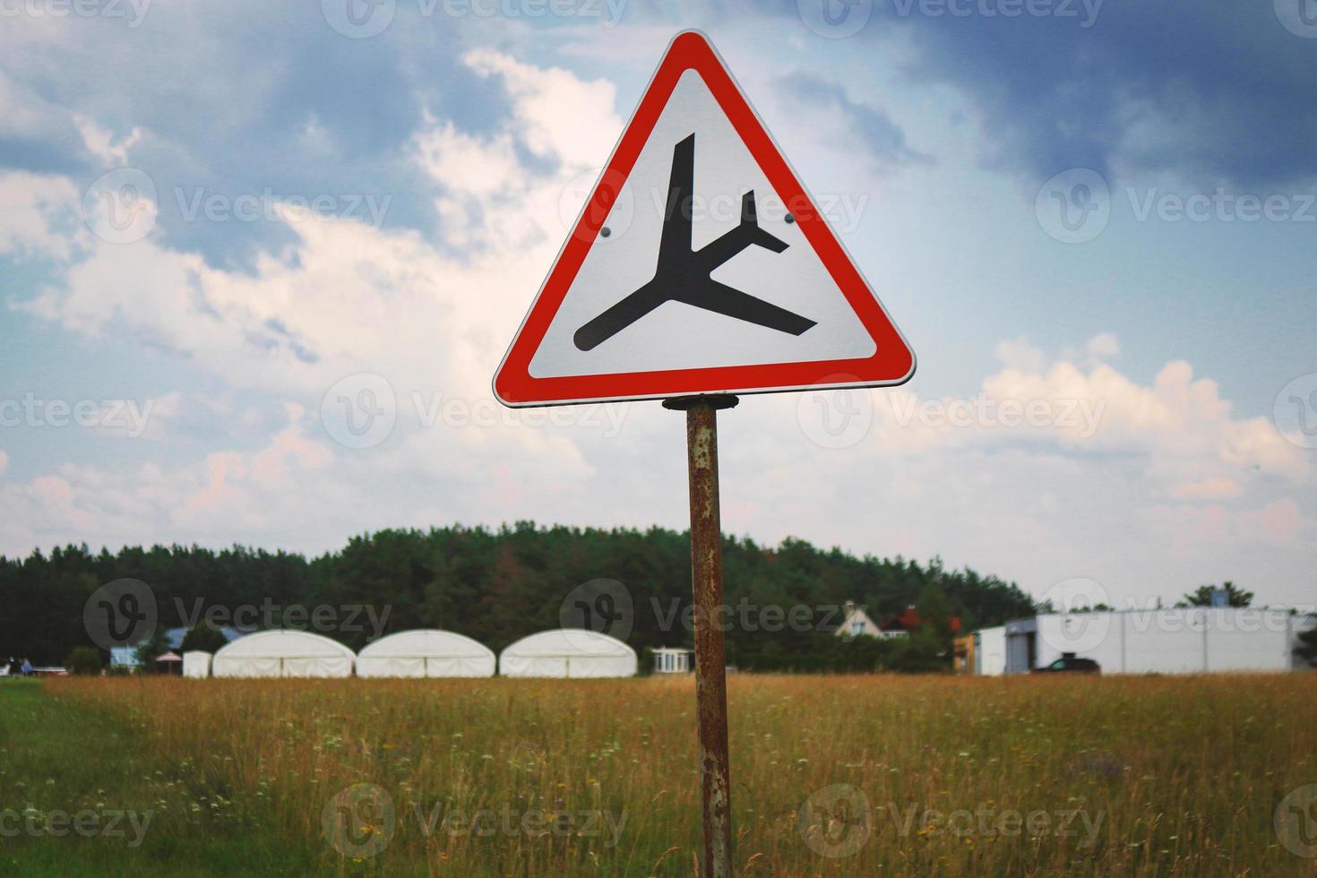 Señal de carretera con triángulo y aterrizaje de avión de pie en el campo en el cielo foto