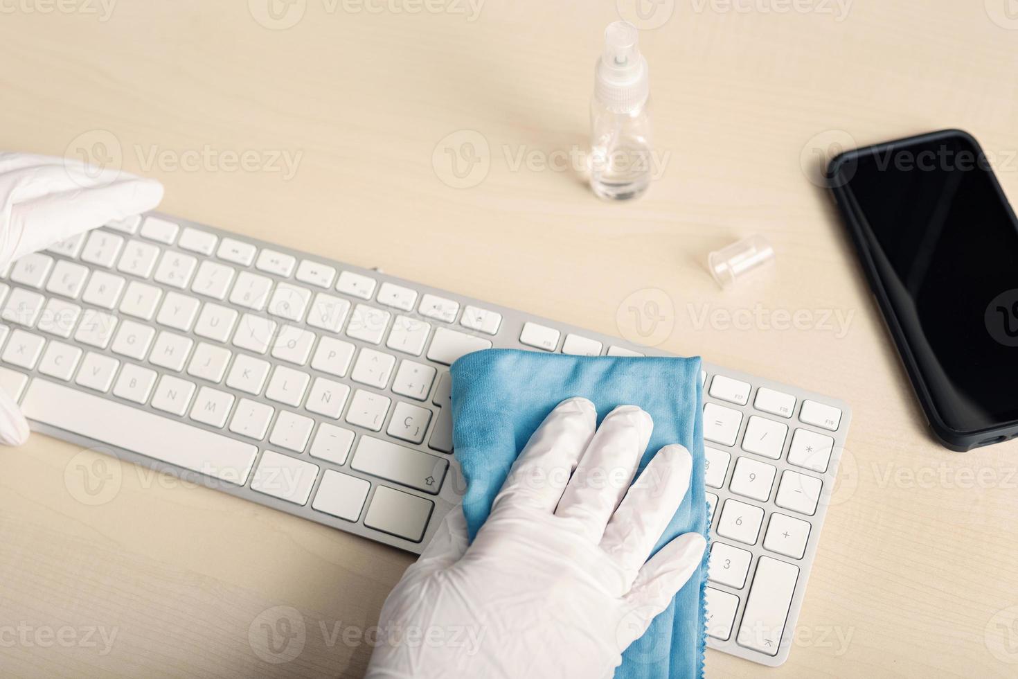 Hand with protective glove cleaning a keyboard with disinfectant photo