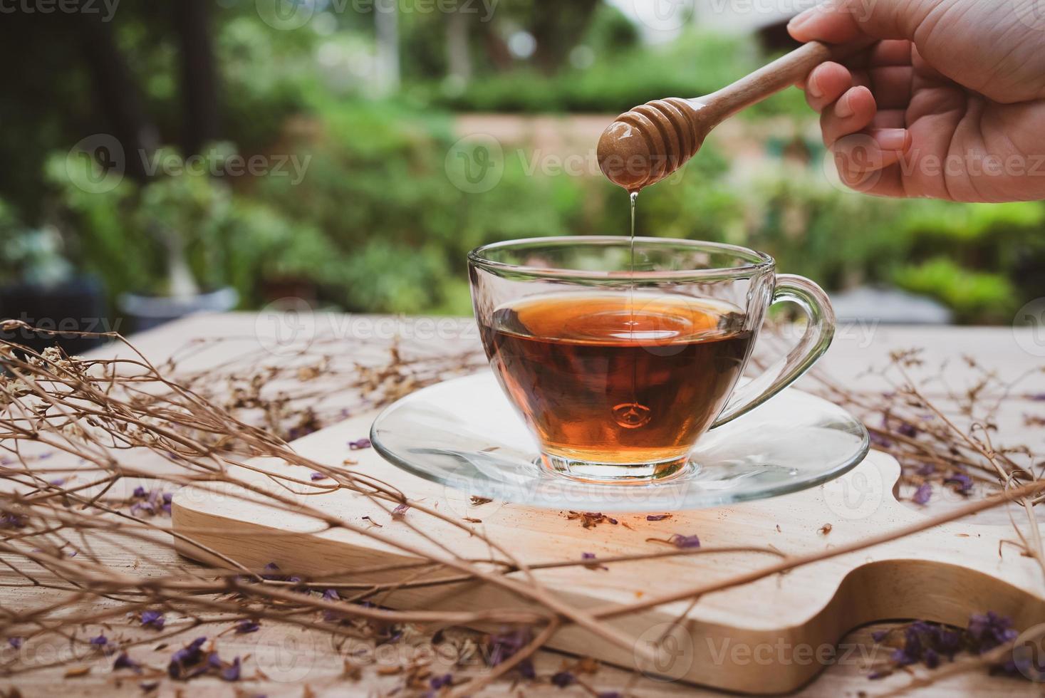 Cerrar mano agregue miel en galss de té caliente foto