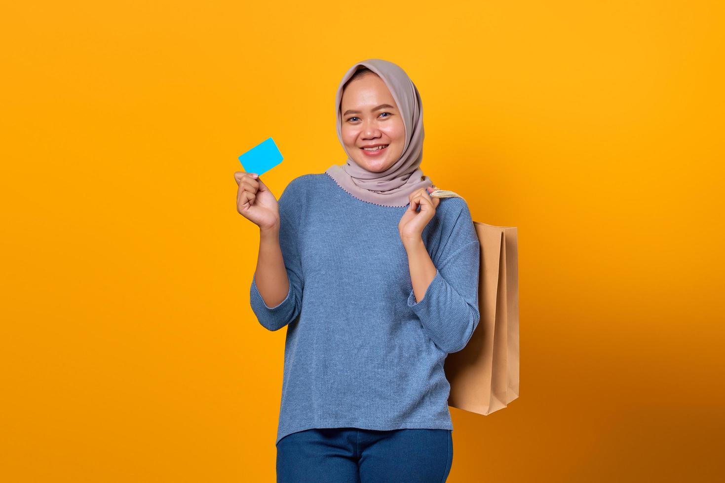 Cheerful Asian woman holding shopping bag and showing credit card photo