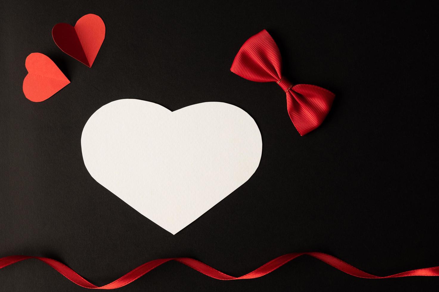 A white heart, a bow, a ribbon, and a red heart are placed photo