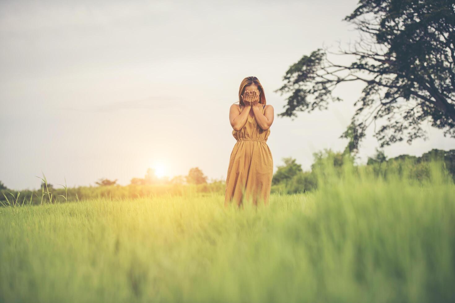 Tristeza mujer de pie con la mano cubriendo su rostro en el campo de hierba foto