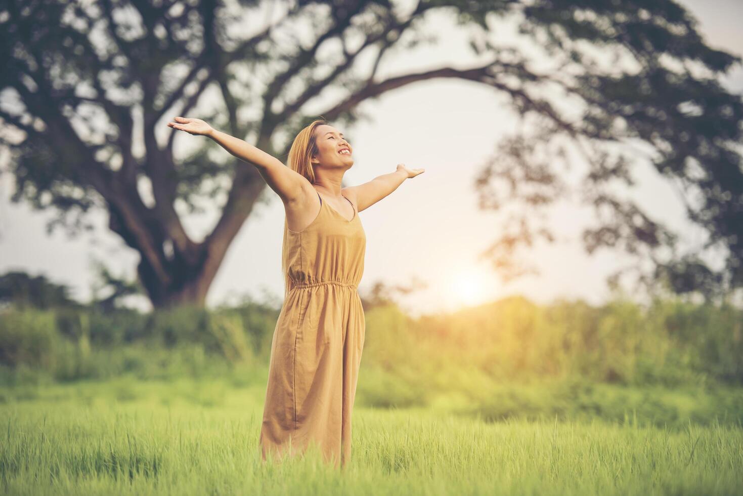 Young woman standing in grass field raising hands in the air. photo