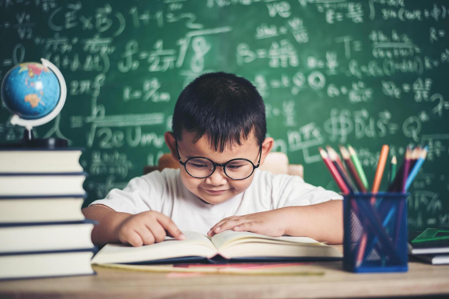 niño leyendo un libro sentado a la mesa en el aula foto