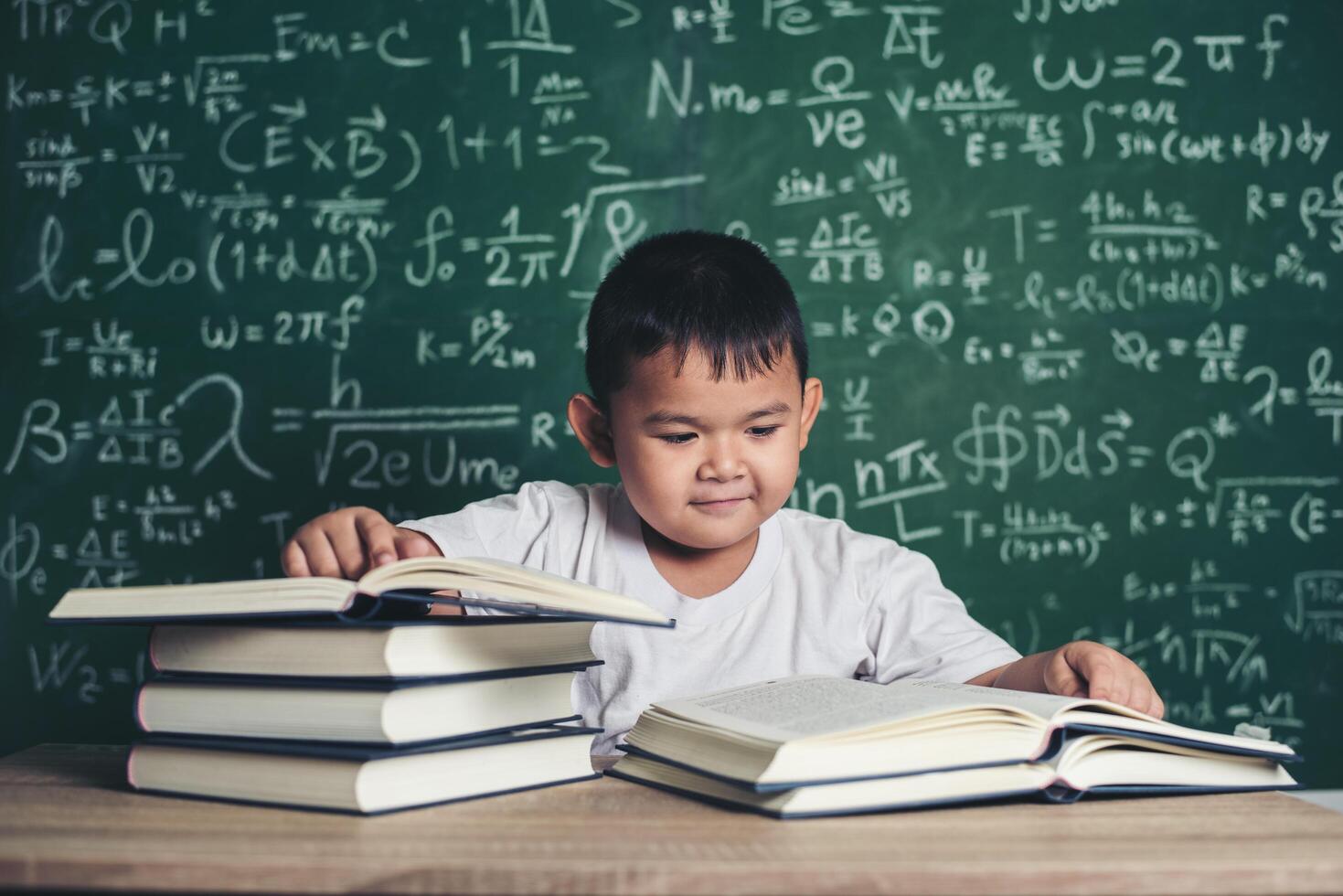 niño leyendo un libro sentado a la mesa en el aula foto