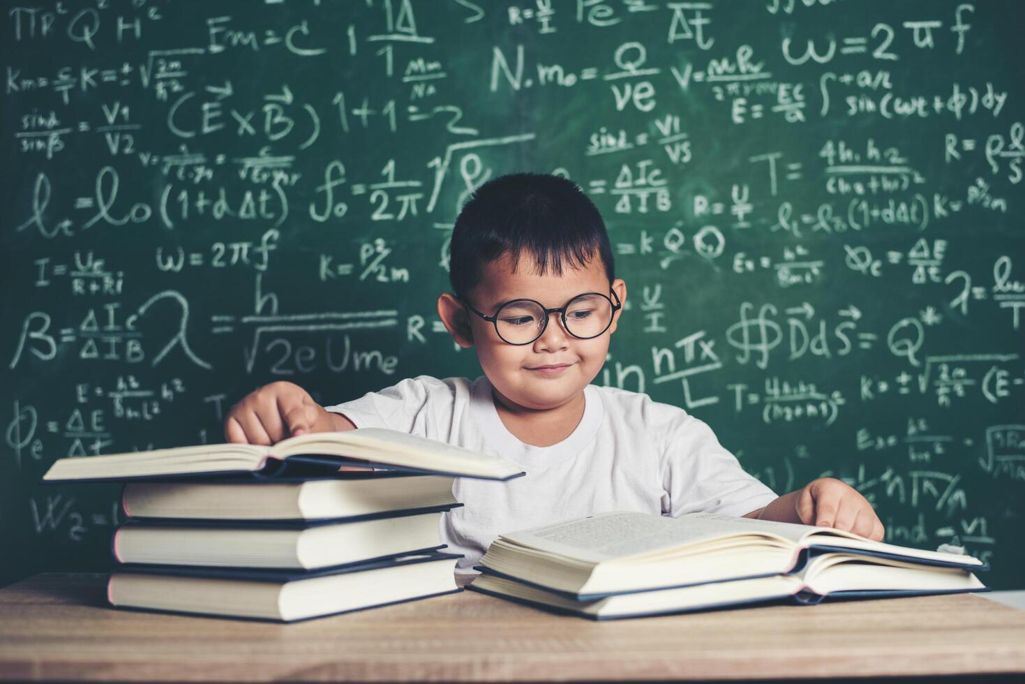 niño leyendo un libro sentado a la mesa en el aula foto