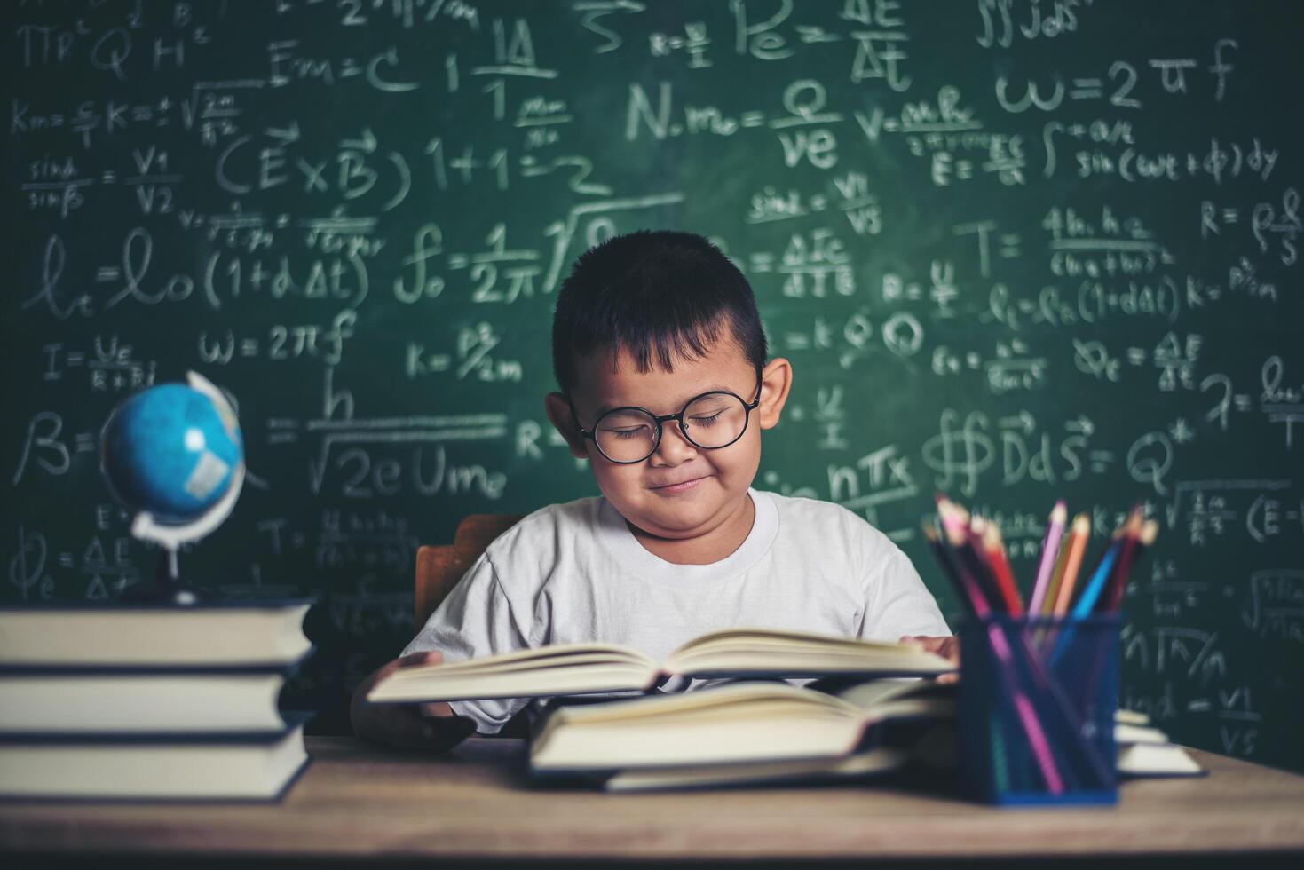 niño leyendo un libro sentado a la mesa en el aula foto