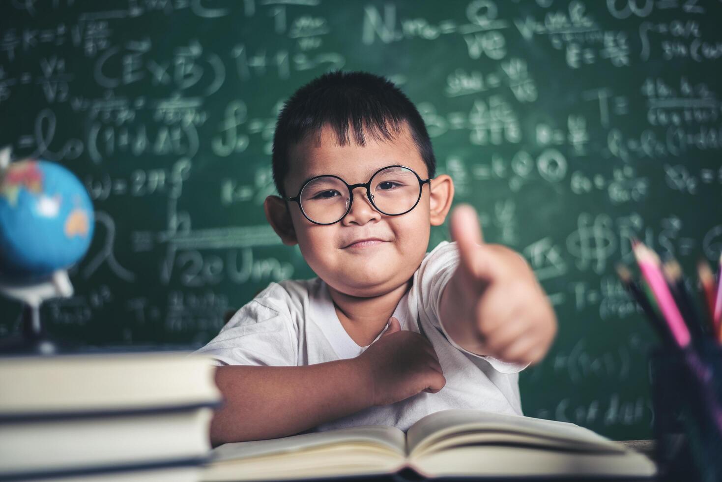 Portrait of a boy with hands thumbs up in the classroom. photo