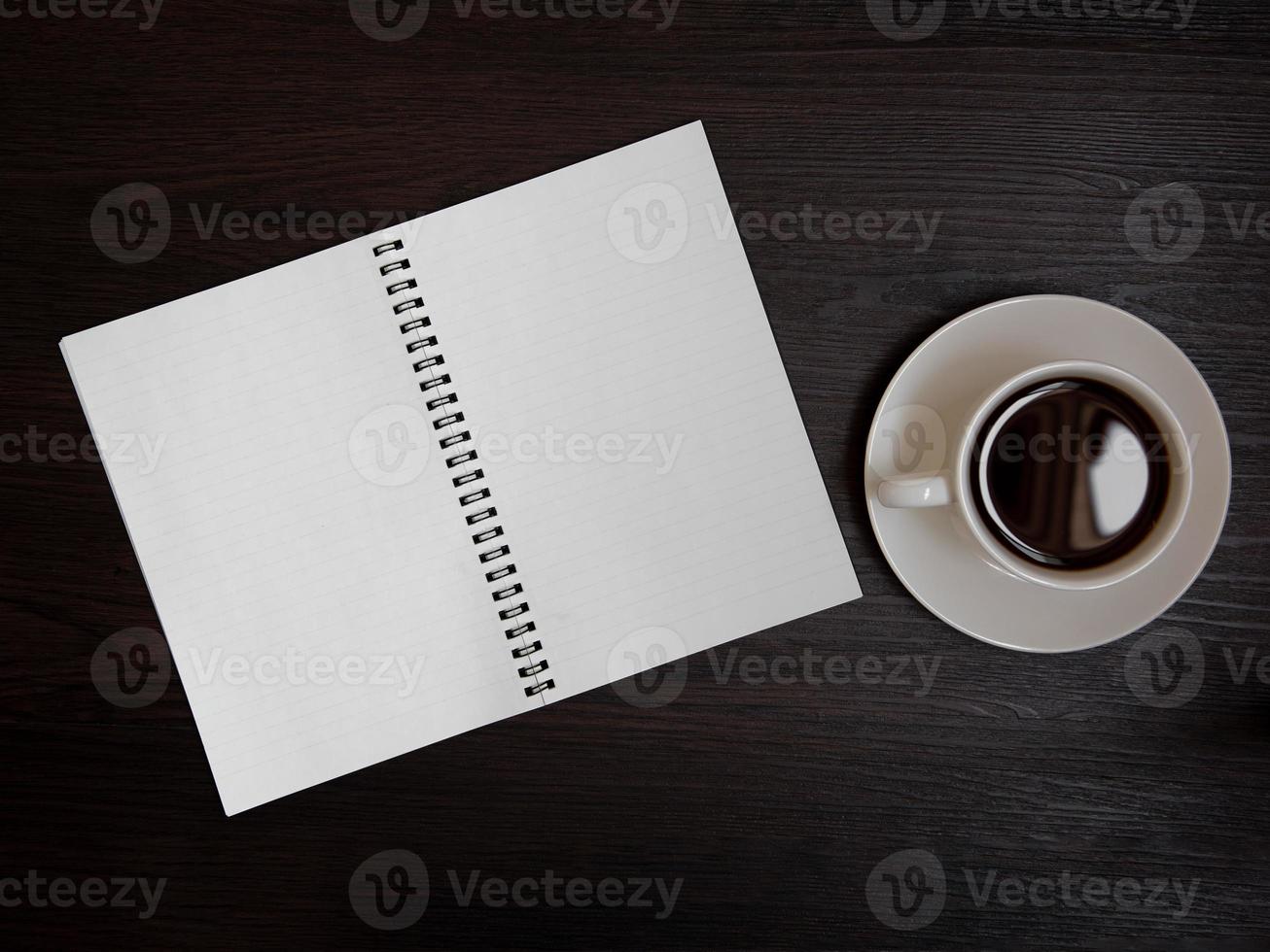 Vista superior de la taza de café y el cuaderno en blanco para memo en la mesa de madera foto