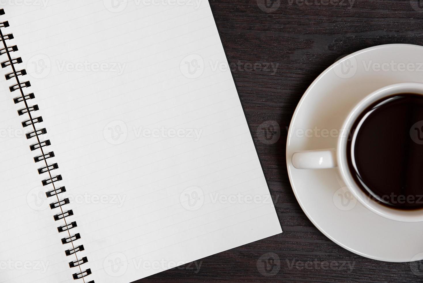 Vista superior de la taza de café y un cuaderno en blanco para notas sobre un piso de madera foto