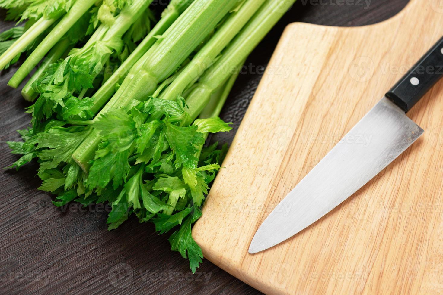 Bunch of fresh celery stalk on wooden table and cutting board photo