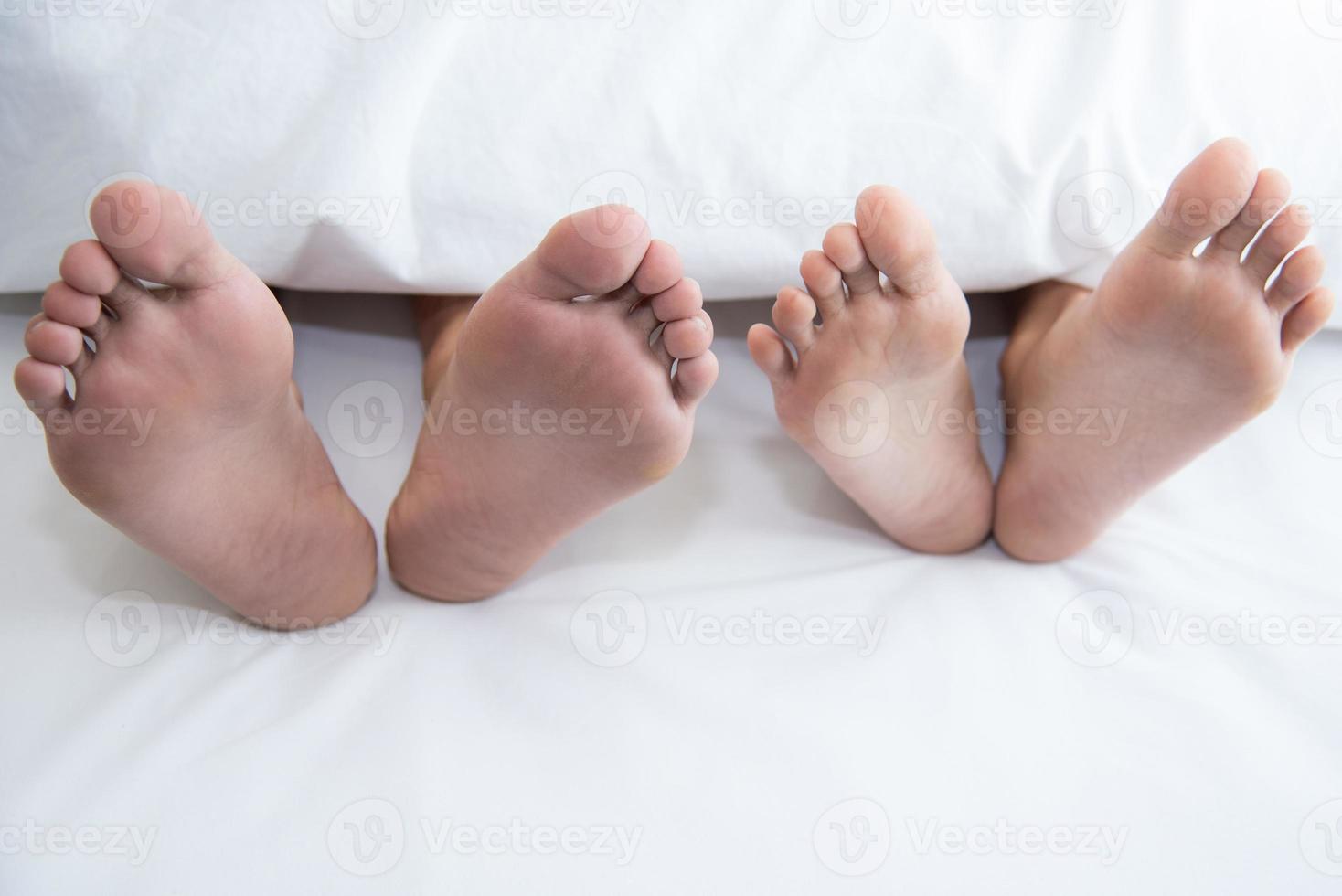 Close up of couple barefoot under blanket in bedroom in honeymoon photo