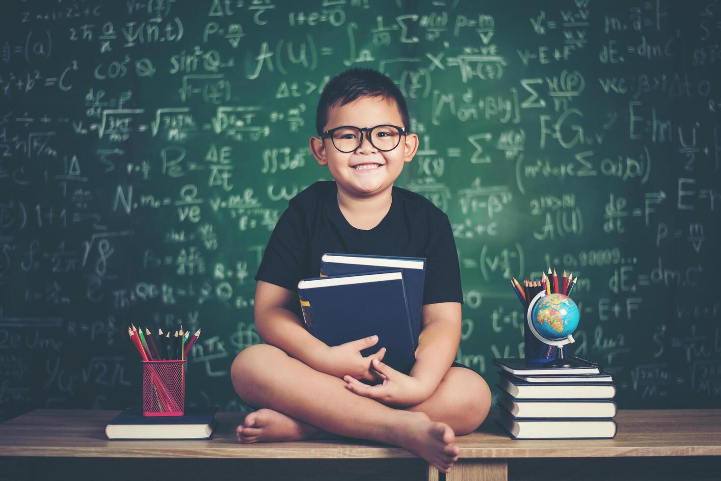 niño con libros sentado cerca de la pizarra verde foto