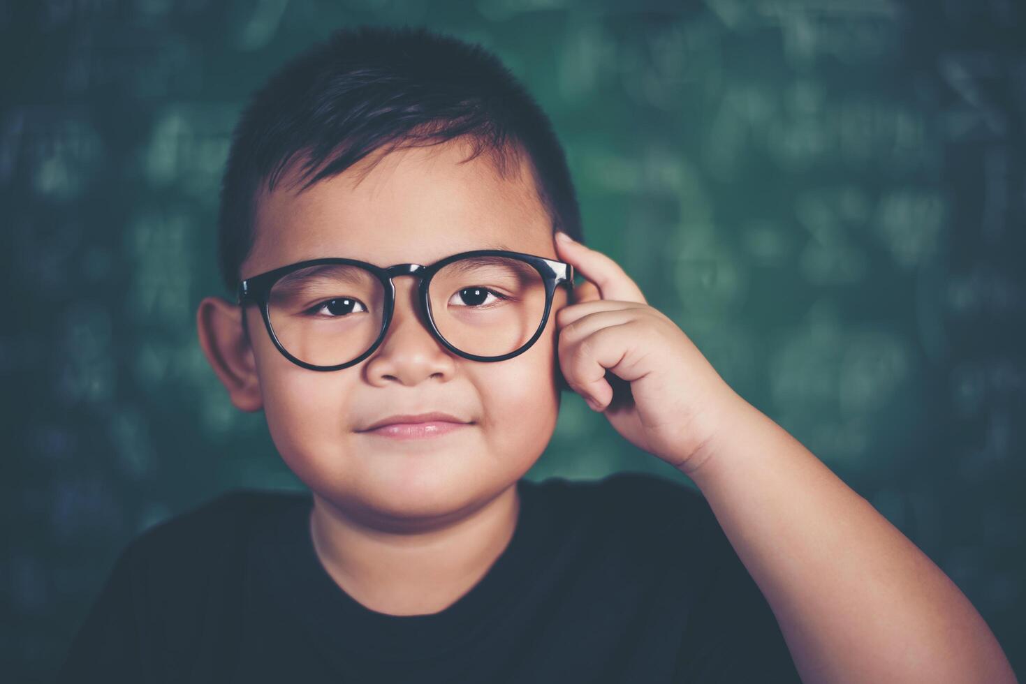 Thoughtful little boy with book near a school board photo