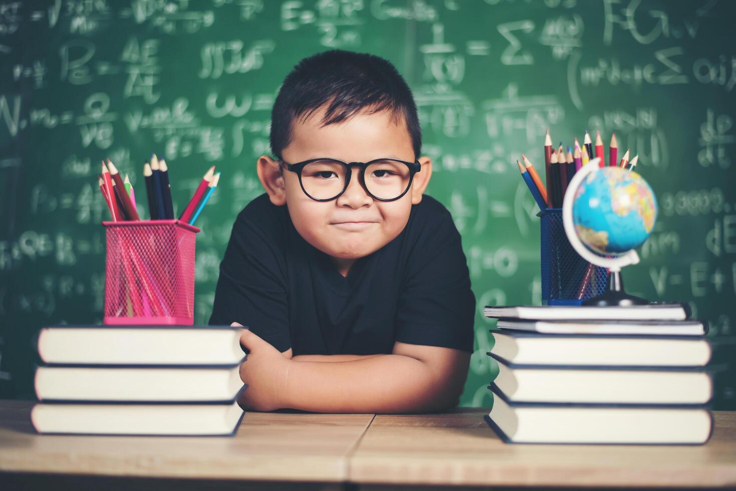 Thoughtful little boy with book near a school board photo