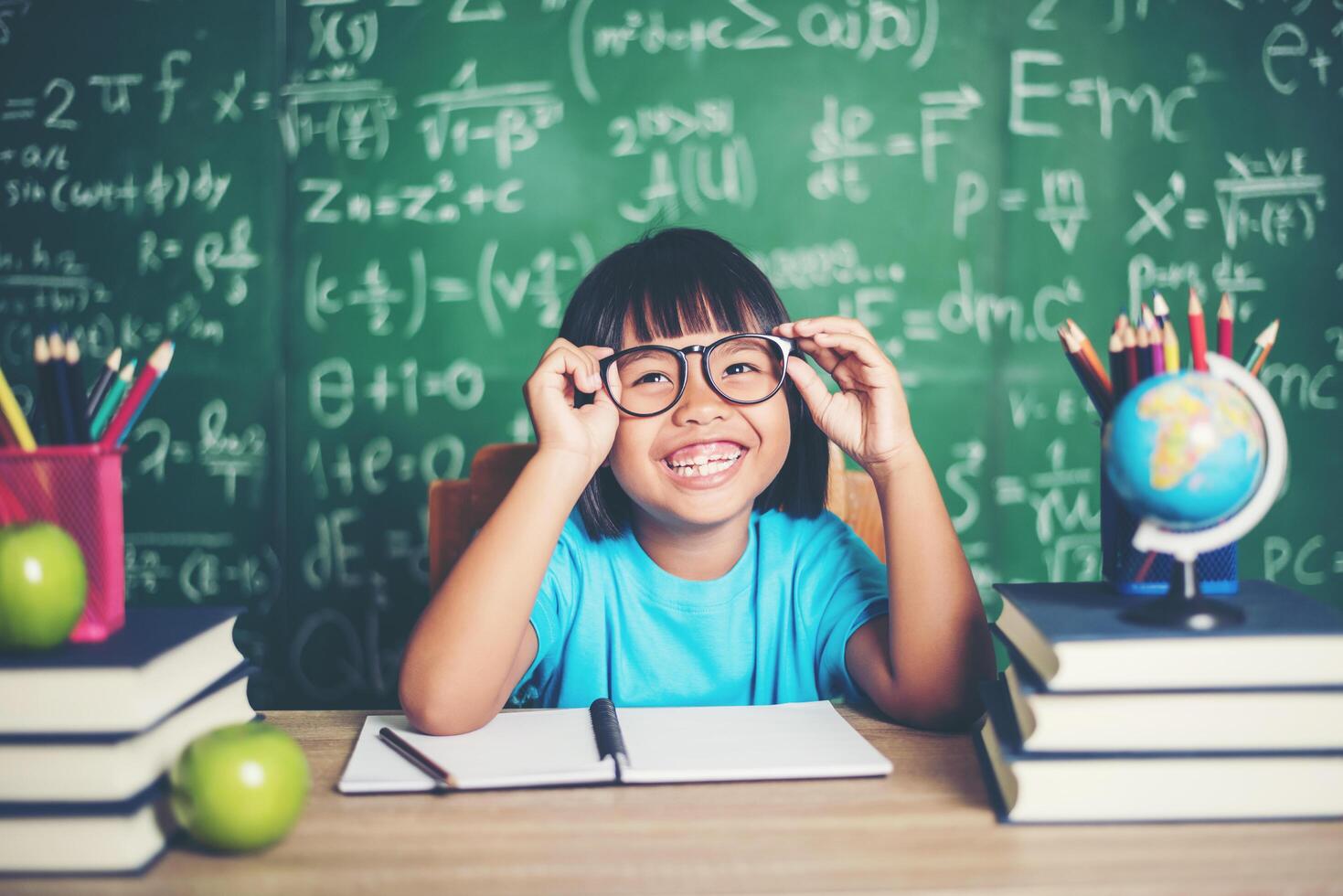 Retrato de colegiala sonriente sentado a la mesa con libros foto